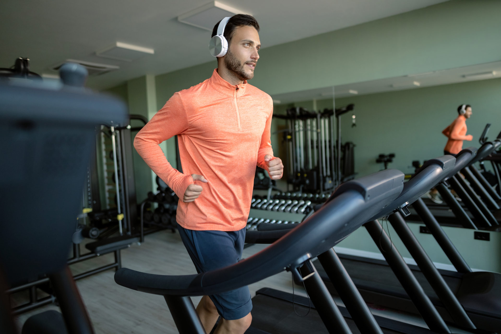 Determined athlete with headphones running on treadmill in a gym.